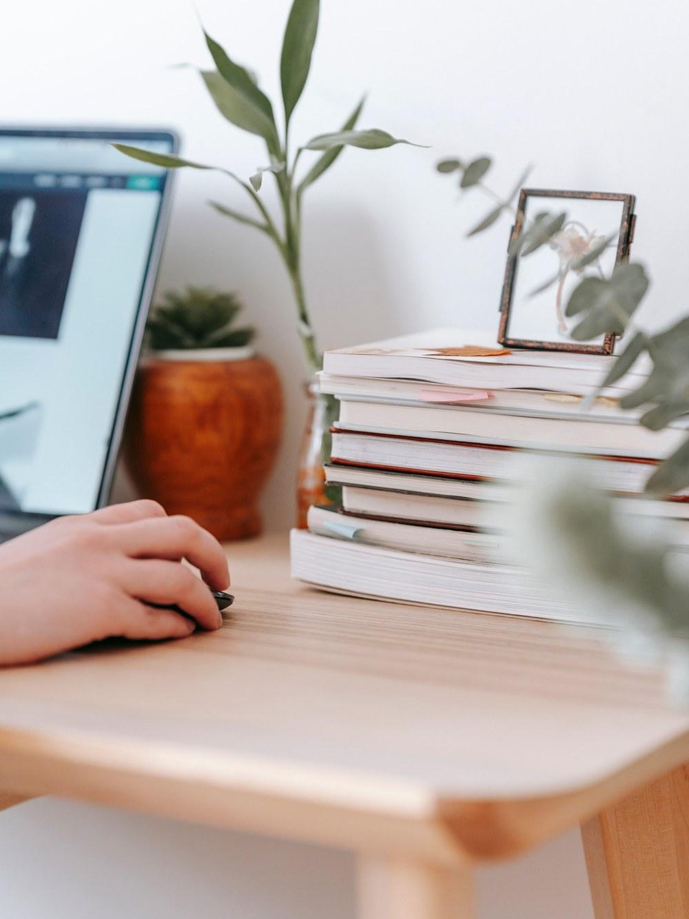 A desk with plants, books, and a hand at a computer mouse